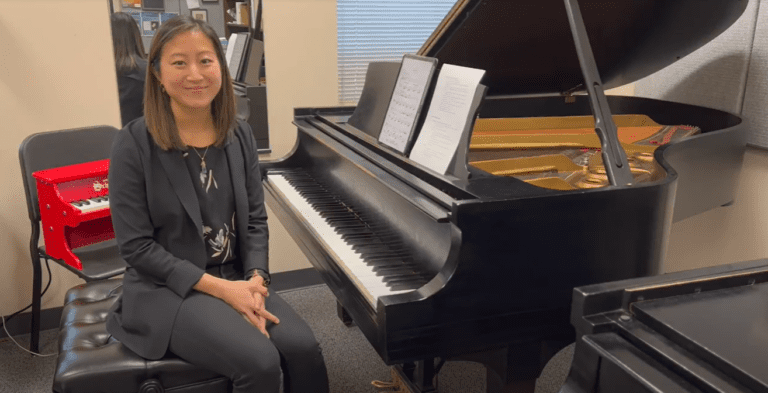 Annie Jeng is sitting at a grand piano and smiling in her introduction.