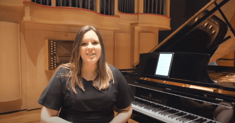 Megan Rich Blood sits on stage in front of a grand piano to discuss.