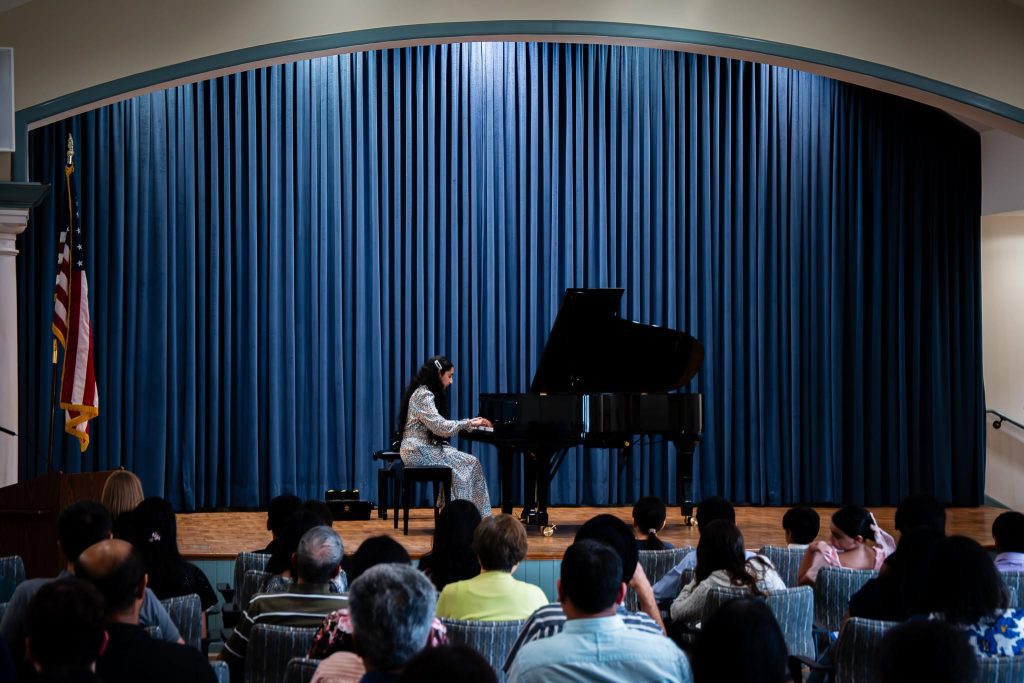 A student from The New School for Music Study performs at the piano for a full audience of attendees.