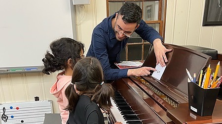 An instructor helps students at the piano with rhythm reading.
