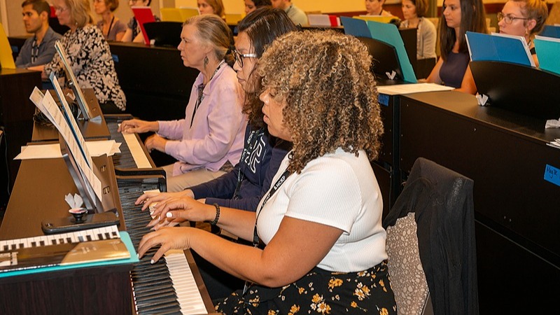 A photo showing a group piano classroom with a diverse student group.