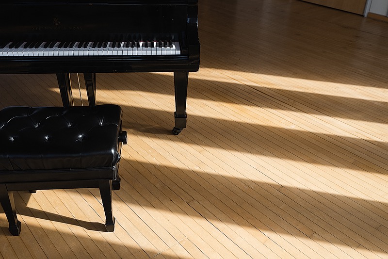 A moody image featuring a grand piano in a dark room with vertical window panes.